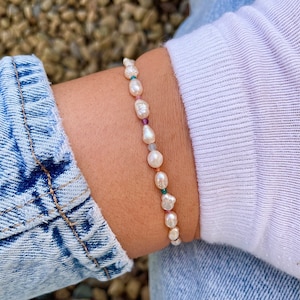 May include: A delicate bracelet featuring a string of white pearls and colourful gemstones. The bracelet is made with natural materials and has a simple, elegant design.