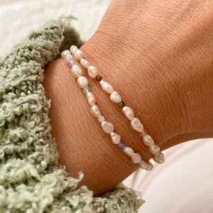 May include: Two delicate bracelets with white pearls and small colorful beads. The bracelets are layered on a person's wrist.