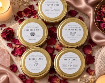 May include: Five round gold-coloured metal tins of massage wax candles with white labels. The labels feature the brand name Kreative Vibrations and the scent names Velvet Lush, Cashmere Kiss, Crowned Flame, Blush Flame, and Naked Flame.