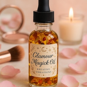 May include: A clear glass bottle of "Glamour Magick Oil" with a black dropper top. The bottle contains amber-colored liquid with small, reddish-brown particles. The label features the text "Glamour Magick Oil" and "Kreative Vibrations". Pink rose petals surround the bottle.
