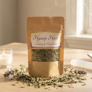 Könnte beinhalten: Ein brauner Papiertüte mit Hyssop-Kraut mit einem transparenten Fenster, beschriftet mit "Hyssop Herb - Cleansing & Purification". Eine brennende Kerze, Räucherstäbchen und ein Selenitstab sind ebenfalls vorhanden. Getrocknete Kräuter und Lavendelzweige liegen auf der Holzoberfläche.
