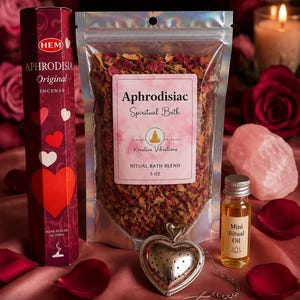 Może przedstawiać: Zestaw rytualny Aphrodisiac zawierający sześciokątne pudełko kadzidełek Hem Aphrodisia, 5-uncjową torebkę mieszanki do kąpieli rytualnej Aphrodisiac Spiritual Bath, małą buteleczkę olejku rytualnego oraz srebrny metalowy zaparzacz w kształcie serca.