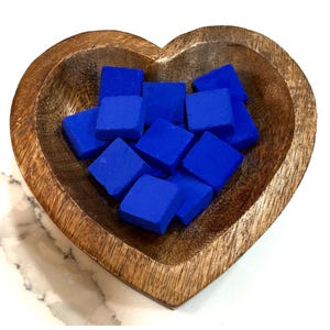 May include: A wooden heart-shaped bowl filled with small, square, cobalt blue objects. The bowl has a natural wood grain finish. The blue squares are evenly distributed within the bowl, creating a visually appealing contrast.
