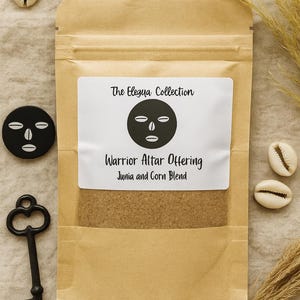 Puede incluir: Una bolsa de papel marrón con una etiqueta blanca que dice "The Elegua Collection" y "Warrior Altar Offering Junia and Corn Blend". La imagen incluye un objeto circular negro con un diseño de cara, una llave vintage y conchas marinas.