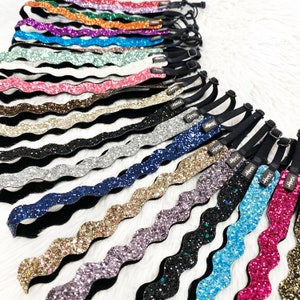 May include: A collection of 20 colorful glitter headbands with a wavy design. Each headband has a black elastic band.