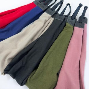 May include: A collection of six fabric headbands arranged in a fan shape, featuring solid colors including red, navy blue, beige, black, olive green, and dusty rose. Each headband has a black adjustable strap with a plastic slider and connector.