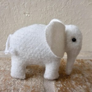 May include: A white plush elephant toy with a black eye. The elephant is made of soft, fuzzy fabric and has a long trunk.