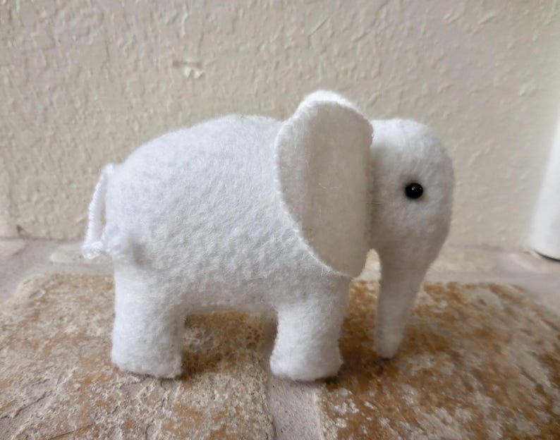 May include: A white plush elephant toy with a black eye. The elephant is made of soft, fuzzy fabric and has a long trunk.