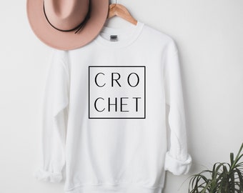 Op de afbeelding: Witte longsleeve trui met zwarte tekst die "CROCHET" binnen een zwart vierkant leest.