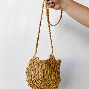 May include: A small, tan, crocheted bag with a scalloped edge and a long, tan strap.