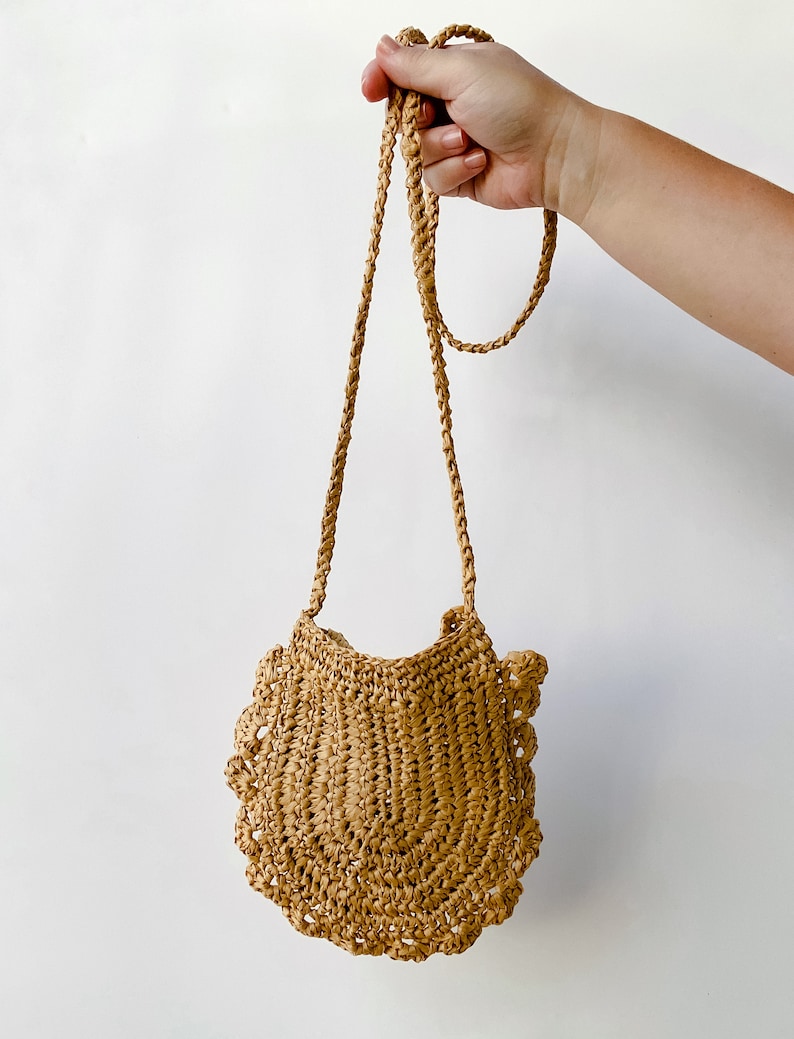 May include: A small, tan, crocheted bag with a scalloped edge and a long, tan strap.