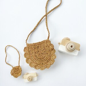 May include: Two small wooden toy cameras and a brown crocheted bag with a long strap. The bag has a scalloped edge.