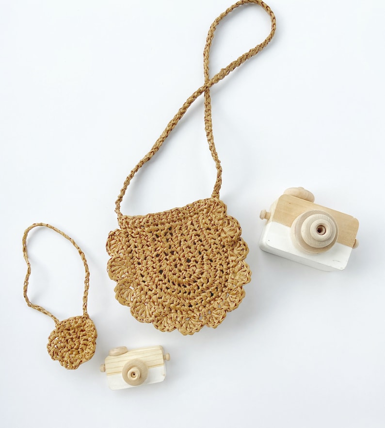 May include: Two small wooden toy cameras and a brown crocheted bag with a long strap. The bag has a scalloped edge.