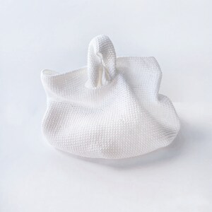 May include: A white crocheted tote bag with a knotted handle.