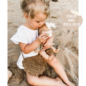 May include: A young child holding a doll with a wooden camera. The child is wearing a white dress and a brown crocheted bag. The doll is wearing a white dress and a brown crocheted bag. The text "CHILD AND DOLL SIZE" is in the background.