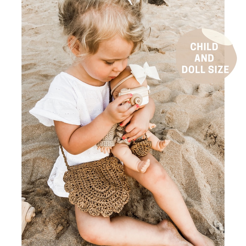 May include: A young child holding a doll with a wooden camera. The child is wearing a white dress and a brown crocheted bag. The doll is wearing a white dress and a brown crocheted bag. The text "CHILD AND DOLL SIZE" is in the background.