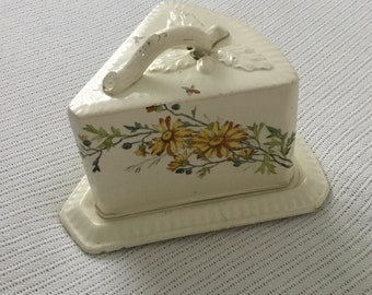 May include: White ceramic cheese dish with a floral design. The dish is shaped like a wedge of cheese and has a handle.