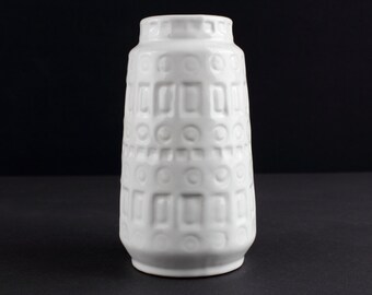 May include: White ceramic vase with a geometric embossed pattern. The vase has a cylindrical shape with a slightly flared opening.