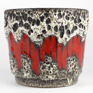 Könnte beinhalten: Ein Keramik-Pflanzgefäß mit strukturierter Oberfläche. Der obere Bereich ist schwarz und weiß, mit einem porösen, lavaartigen Aussehen. Der mittlere Bereich weist vertikale rote Streifen auf. Der Sockel ist dunkelgrau.