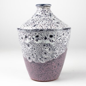 Puede incluir: Un jarrón de cerámica blanco y morado con un esmalte moteado. El jarrón tiene un cuerpo redondeado y un cuello estrecho.