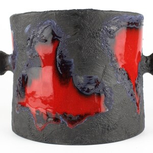 May include: A black ceramic planter with two handles and a red glaze. The glaze has a textured, lava-like appearance.