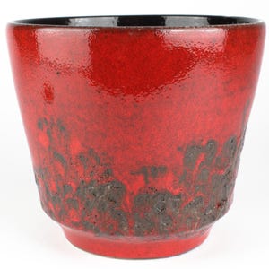 Op de afbeelding: Een levendige rode keramische bloempot met een getextureerde, donkerbruine onderkant. De binnenrand is zwart en de pot heeft een licht uitlopende vorm. Deze decoratieve pot is geschikt voor binnen of buiten.