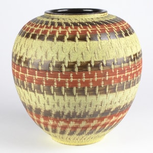 Può includere: Un vaso rotondo in ceramica con un motivo geometrico in tonalità di marrone, giallo e rosso.