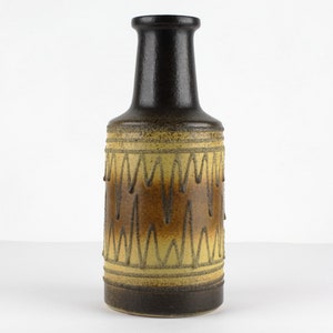 Può includere: Un vaso in ceramica marrone e giallo con un motivo geometrico. Il vaso ha un collo stretto e una base larga.