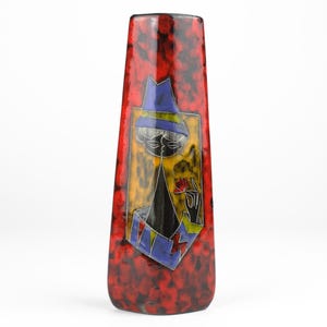 May include: A red ceramic vase with a stylized black and white figure wearing a blue hat and holding a red flower. The vase has a speckled red glaze.