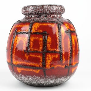 Può includere: Un vaso vintage in ceramica dalla forma bulbosa e dalla superficie strutturata. Il vaso presenta un sorprendente design di motivi geometrici rossi e arancioni delineati in nero. Il bordo e la base hanno una finitura maculata marrone scuro.