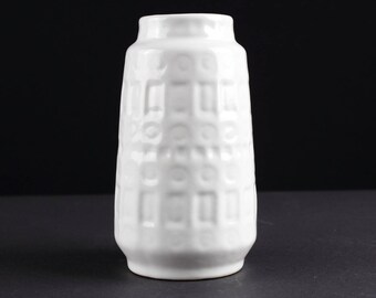 May include: White ceramic vase with a textured, geometric pattern. The vase is tall and slender, with a rounded base and a slightly flared opening.
