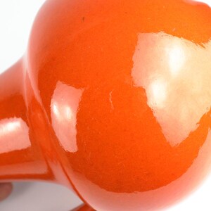 May include: Close-up of a vintage orange hair dryer. The hair dryer has a rounded head and a long, tapered handle. The glossy finish reflects light, highlighting its retro design.