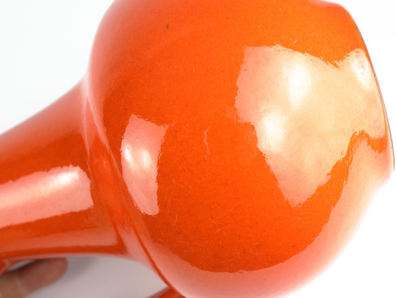 May include: Close-up of a vintage orange hair dryer. The hair dryer has a rounded head and a long, tapered handle. The glossy finish reflects light, highlighting its retro design.