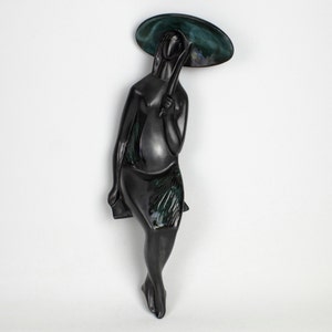 May include: Black ceramic sculpture of a person holding an umbrella. The sculpture is glazed in a dark green and black colour.