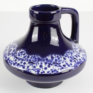 Könnte beinhalten: Eine blaue Keramikvase mit einem weißen, gesprenkelten Design. Die Vase hat einen breiten Boden und einen schmalen Hals mit einem Henkel.