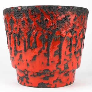Può includere: Vaso in ceramica rosso con smalto nero strutturato. Il vaso ha una forma cilindrica con un bordo leggermente svasato e una superficie strutturata. Ideale per piante da interno, circa 15 cm di altezza.