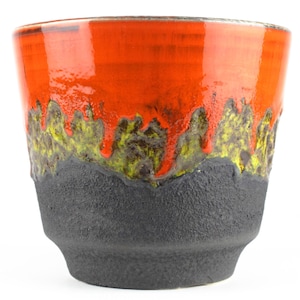 Pode incluir: Um vaso de cerâmica com base preta e um esmalte laranja brilhante com um design de gotejamento verde e marrom.