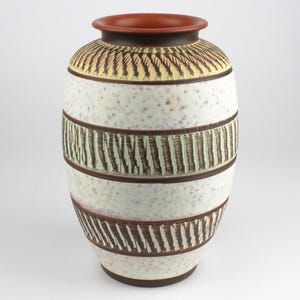 Peut inclure: Un vase en céramique blanche avec des motifs géométriques bruns et verts. Le vase a une large ouverture et un corps arrondi.