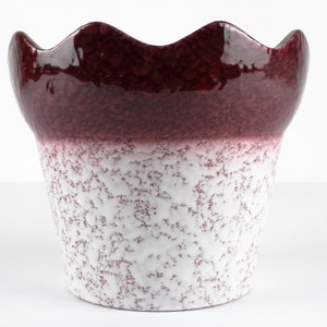 Puede incluir: Una maceta de cerámica blanca y burdeos con un borde ondulado. La maceta tiene un esmalte moteado.
