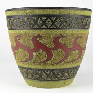 Könnte beinhalten: Ein großer, grüner Keramiktopf mit strukturierter Oberfläche. Er hat ein schwarzes und rotes geometrisches Design um die Mitte.
