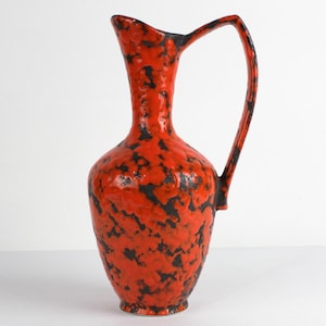 Puede incluir: Un jarrón de cerámica rojo y negro con una superficie texturizada y un asa. El jarrón tiene la forma de una jarra.