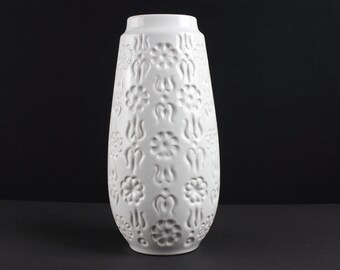 May include: White ceramic vase with an embossed floral pattern. The vase is tall and slender with a rounded base.