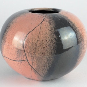 Könnte beinhalten: Eine runde Keramikvase mit rosa und schwarzer Glasur. Die Vase hat eine craquelée Oberfläche und einen glänzenden Glanz.
