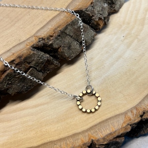 May include: A silver chain necklace with a gold circle pendant. The circle is made of small, round beads.