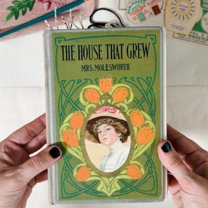 Op de afbeelding: Een vintage hardcover boek getiteld The House That Grew door Mrs. Molesworth. De groene kaft bevat een ovale illustratie van een persoon met een hoed, omringd door een decoratieve rand van oranje tulpen en gedetailleerde groene lijnpatronen.