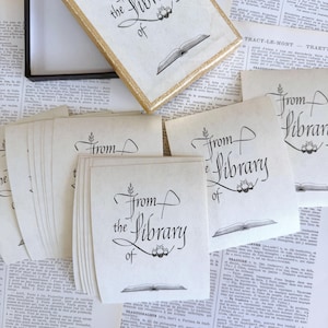 May include: A set of cream-coloured library cards and a decorative box with gold trim. The cards and box feature the text "From the Library of" in elegant black script, along with an open book illustration.