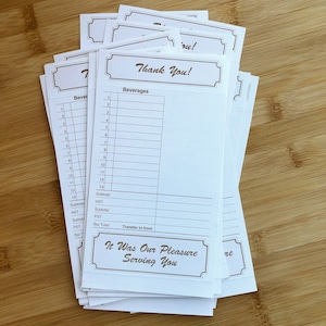 May include: A stack of white paper thank you receipts with brown text. The top receipt has the words "Thank You!" in a brown rectangle. The receipt has a section for beverages with numbered lines for listing items. The bottom of the receipt has the words "It Was Our Pleasure Serving You" in a brown rectangle.