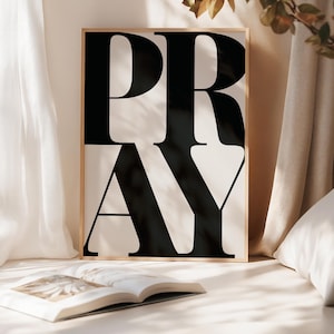 Modern Christian wall art print with the word ‘PRAY’ in bold black typography on a white background in a prayer space, soft neutral bedroom decor. statement wall art piece for faith-filled homes. Scripture print poster for prayer rooms and church spaces.