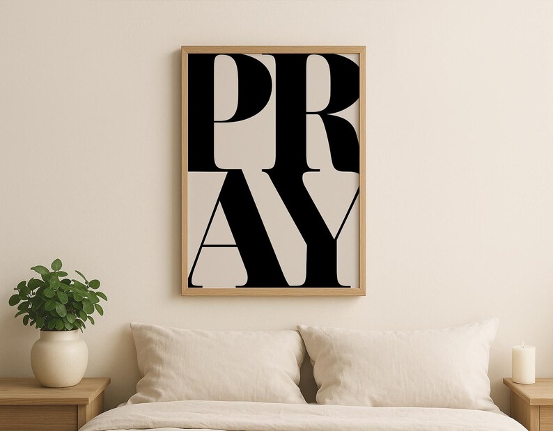 Faith-based home decor print with PRAY lettering, displayed in a modern living room with plants and a candle