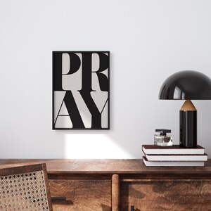 Minimalist PRAY typography wall art in a white frame, styled above a wooden desk in a minimalist, clean, tidy home office space